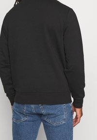 Felpa nera con maniche lunghe, orlo a coste e texture liscia. Abbinata a jeans in denim blu con un aspetto sbiadito e tasche.