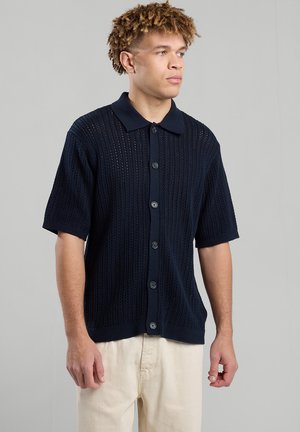 Camicetta navy in maglia a maniche corte con chiusura a bottoni, caratterizzata da un motivo testurizzato e un design del colletto classico.