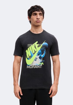 Νέος άνδρας φοράει μαύρο T-shirt Nike με τον μπασκετμπολίστα Ja Morant σε μπλε χρώμα με φωτεινό κίτρινο κείμενο και λογότυπο μπροστά.