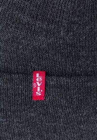 Tissu tricoté gris foncé avec une petite étiquette verticale rouge de la marque Levi’s cousue sur la surface.