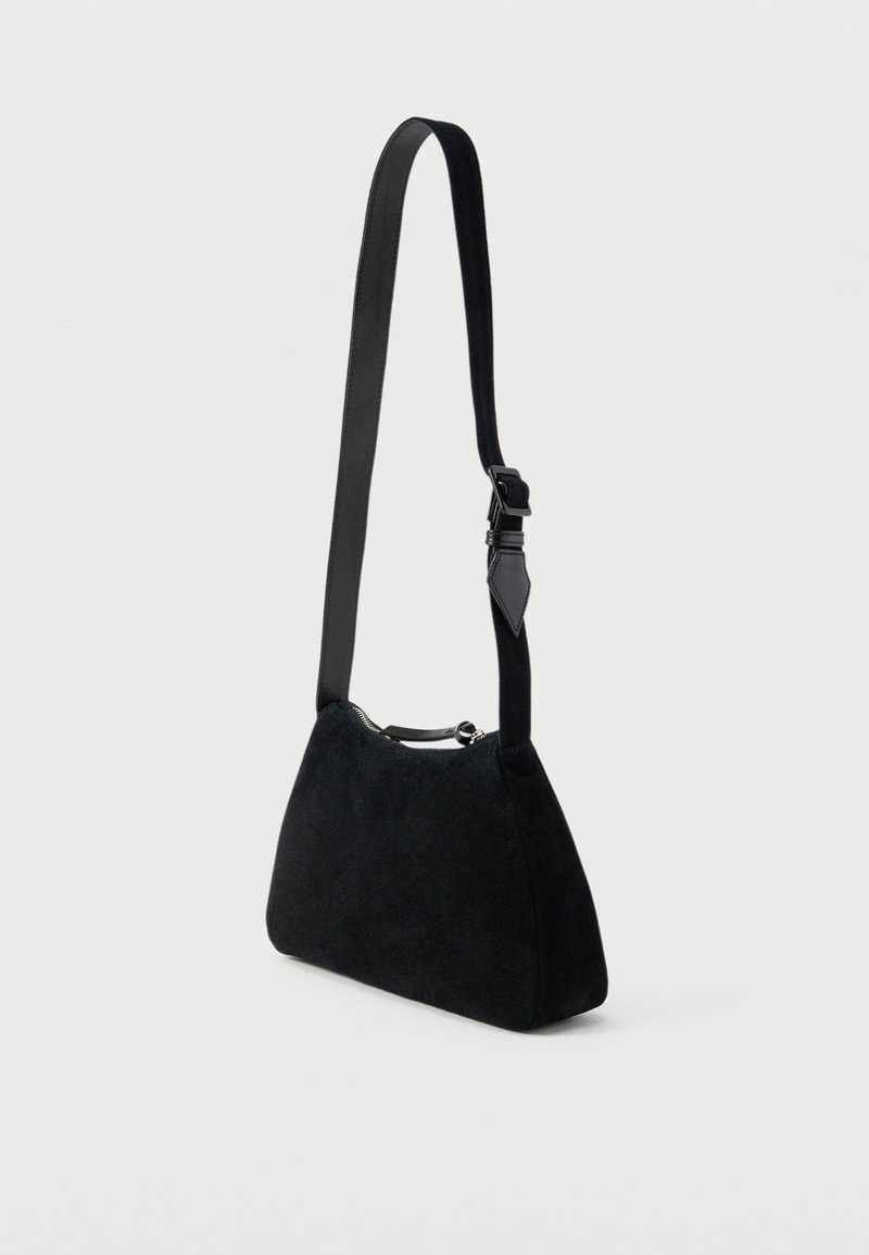 Kleine schwarze Schultertasche aus Wildleder mit verstellbarem schwarzen Lederriemen und silbernem Reißverschluss vor schlicht weißem Hintergrund.