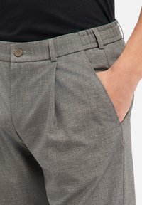 Graue, maßgeschneiderte Hosen mit klassischem Design, vorne mit Biesen, seitlichen Taschen und einem Metallknopfverschluss an der Taille.