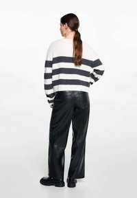 Zkrácený pletený svetr s námořnickými a bílými horizontálními pruhy, spárovaný s černými širokými kalhotami z umělé kůže a robustními černými botami.