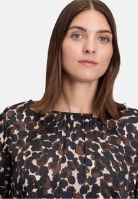 Bedruckte Bluse aus durchsichtigem Stoff mit einem Leopardenmuster in Schwarz, Braun und Creme, runder Ausschnitt und Faltendetails an der Vorderseite.