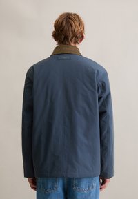 Mornarsko plava, lagana jakna s dugim rukavima i okovratnikom od smeđeg manšestra. Ima ravni kroj i minimalistički dizajn.