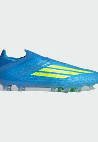 Chaussure de football bleue avec des rayures jaune néon, design sans lacets et crampons translucides sur la semelle, vue de côté.