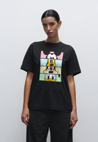 Sort bomuld t-shirt med et tekstureret grafisk motiv af tegneseriefigurer i pastelfarver. Afslappet pasform med korte ærmer og rund hals.