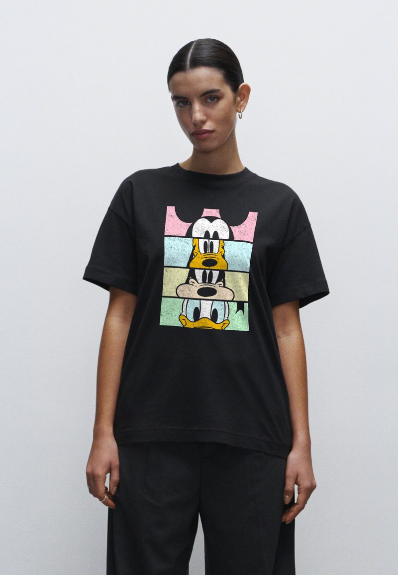 T-shirt nera in cotone con una grafica testurizzata di personaggi dei cartoni animati in colori pastello. Vestibilità rilassata con maniche corte e colletto rotondo.