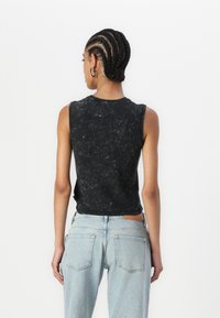Svart ärmlös topp med marmortextur, kombinerad med ljusblå jeans med hög midja försedda med en brun läderetikett på baksidan.