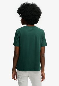 Dunkelgrünes T-Shirt mit kurzen Ärmeln, ausgestattet mit einem Rundhalsausschnitt und einem leicht lockeren Schnitt, gefertigt aus weicher Baumwolle mit glatter Textur.