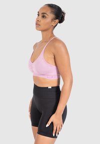 Vaaleanpunainen urheilbra, jossa on säädettävät hihnat ja kerätty keskikohta. Mustat korkeavyötäröiset shortsit, joissa on sileä pinta ja vyötärönauhadetail.