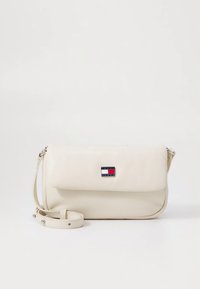 Cream-colored crossbody bag made of smooth material, featuring a flap closure, adjustable strap, and a rectangular logo accent.