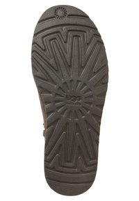 Suela de zapato de goma negra con un patrón geométrico texturizado y un diseño floral central, además de la marca "UGG Australia".