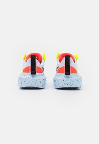 Färgglada sneakers har en vit ovandel med neongr öna inslag, en spräcklig ljusblå sula och svarta dragremmar på baksidan för enkel påtagning.