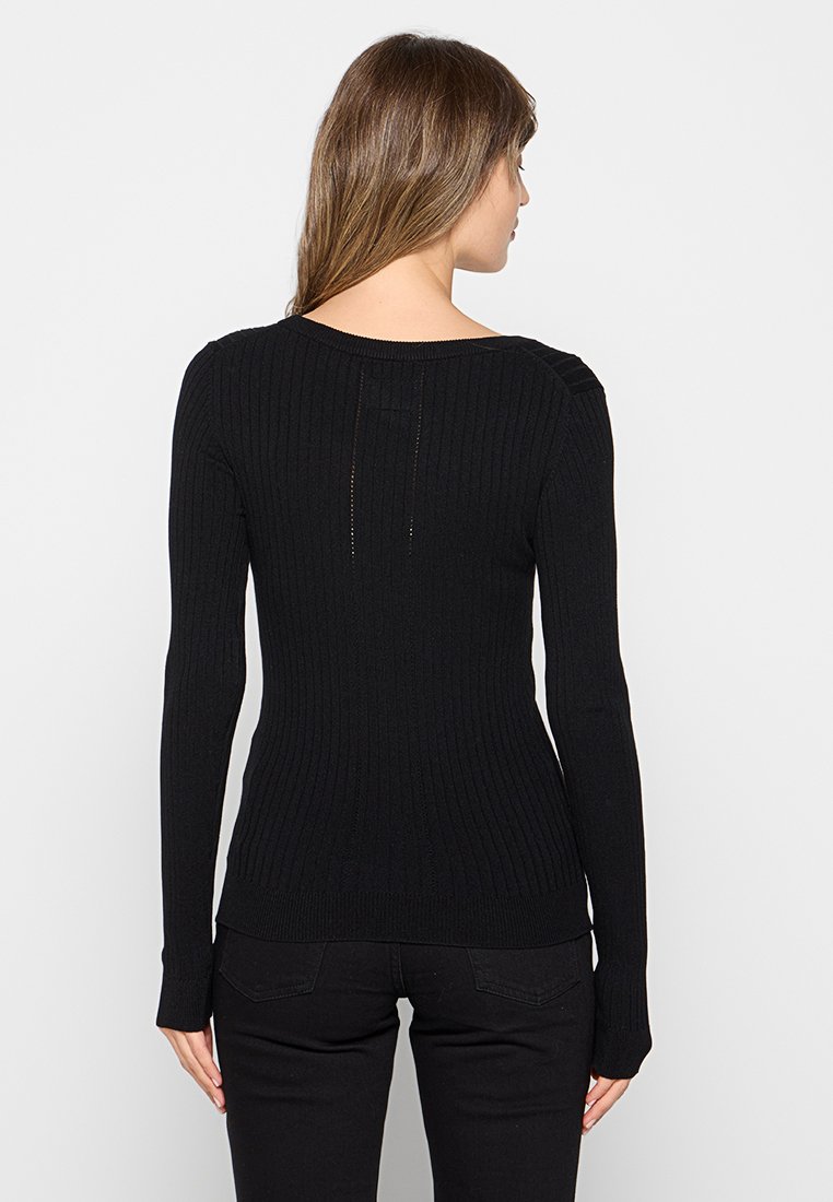 Maglione nero a coste con maniche lunghe e scollatura tonda. Presenta una forma aderente e un sottile dettaglio di cucitura sulle spalle.