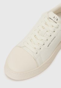 Witte leren sneaker met ronde neus, gestructureerde bovenkant en platte veters. Voorzien van een reliëflogo en een rubberen zool met een gestructureerde rand.