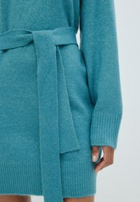 Türkises Strickkleid mit passendem Gürtel. Verfügt über gerippte Bündchen und Saum, strukturierter Stoff und einen leicht lockeren Schnitt.