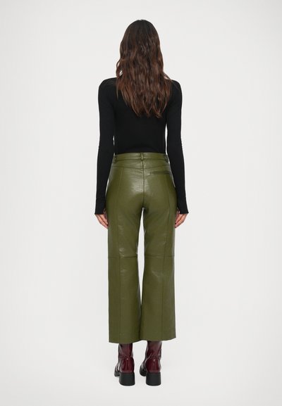 Calças largas de pele sintética verde-oliva com uma textura suave, cintura alta e bolsos traseiros, combinadas com botas burdeos até ao joelho.