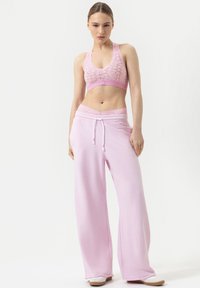 Lichtroze sportset bestaande uit een kanten bralette en wijde sweatpants met een trekband in de taille en textuuraccenten. Eenvoudig ontwerp, zachte textuur.
