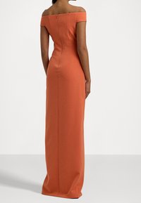 Axelärmad, figursydd klänning i rostorange tyg, med dragkedja i ryggen och en lång, svävande kjol.