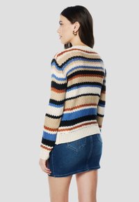 Többszínű kötött pulóver vízszintes csíkokkal, krém, kék, narancs és fekete színekben. Bordázott szegéllyel és testhez simuló szabással. Farmer szoknyával párosítva.