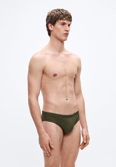 Μαγιό τύπου briefs σε ελιά πράσινο χρώμα, κατασκευασμένα από απαλό ύφασμα, με απλό, εφαρμοστό σχέδιο σε μονόχρωμο χωρίς ορατά μοτίβα ή διακοσμητικά στοιχεία.