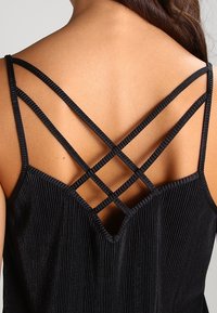 Top tecnico nero con spalline incrociate sul retro, in tessuto a coste e scollatura a V. Le spalline sono sottili e dettagliate.