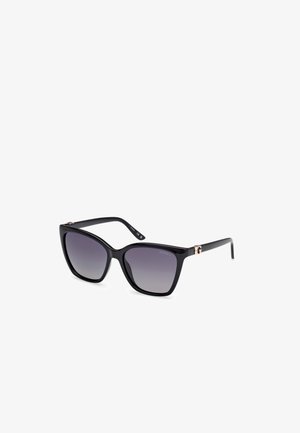 Gafas de sol negras de gran tamaño con lentes degradados, forma angular de gato, montura de plástico brillante y acento en tono dorado con el logo en la patilla.