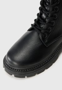 Black lace-up ankle boot featuring a textured leather upper, rounded toe, and a rugged rubber sole with a pronounced tread pattern.