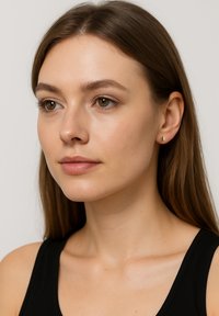 Närbild av en person med medellångt rakt hår. Huden  är ljus och de bär små örhängen i guld. Bakgrunden är neutral.