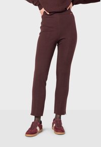 Bordeaux leggings van een elastische stof met een strakke pasvorm en een lichte split bij de enkel, gecombineerd met bordeaux sneakers.