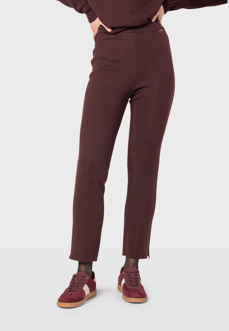 Burgundy leggings i ett stretchigt tyg med en åtsittande form och en lätt delning vid vristen, som matchas med burgundy sneakers.