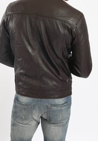 Brun läderjacka med en slät textur, som har en strukturerad design och en figurnära siluett, kombinerad med bleka blå jeans.