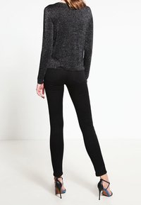 Svart, glittrig långärmad topp i kombination med slim fit svarta jeans och högklackade sandaler, vilket framhäver en figurnära silhuett och strukturerad tyg.