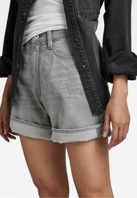 Bermudas de mezclilla gris con dobladillo enrollado, textura ligeramente deslavada, diseño de cinco bolsillos y cierre de botón único, combinadas con una camisa negra de botones.