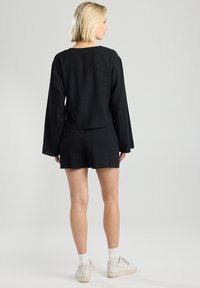 Musta pellavapaita pitkillä hihoilla yhdistettynä mustiin shortsihousuihin. Asusteessa on rento istuvuus ja yksinkertainen muotoilu, jonka kanssa on käytetty valkoisia tennareita ja sukkia.