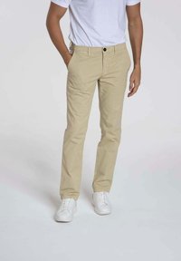 Chinos beige en coton avec une coupe droite, dotés d'une fermeture à bouton et de poches latérales, associés à des baskets blanches.