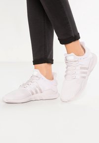 Vita träningsskor med mesh-övre, vadderad krage och gummisula; har tre horisontella ränder på sidan för varumärkesidentifiering.