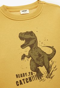 Żółta bluza z nadrukiem ilustracji T. rexa oraz tekstem "GOTOWY NA ZŁOWIENIE!!!". Materiał jest żebrowany przy kołnierzy i mankietach.