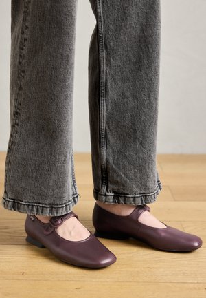 Mary Jane zābaki tumši bordo ādas, ar noapaļotu purngalu, maigu sprādzi un zemu blokveida papēdi, kombinēti ar pelēkiem plaša griezuma džinsiem.