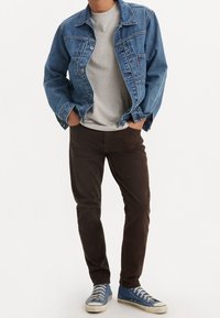 Giacca di jeans blu scuro, t-shirt grigia, pantaloni in corduroy marroni e sneakers blu con suole bianche. Outfit casual con texture sovrapposte.