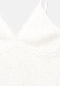 Vit ärmlös topp med en texturerad, krinklad tyg. Har en djup V-ringning och dekorativ spetsbård längs kanterna.