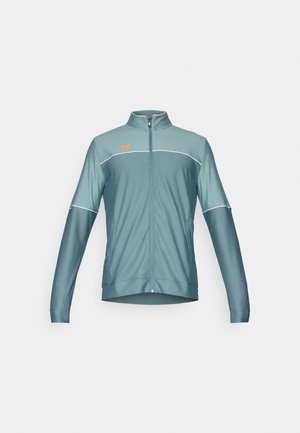 Grønn atletisk zip-up jakke med lange ermer, med stående krage, hvite detaljer og en oransje logo. Myk, glatt stofftekstur.