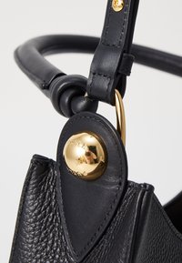 Zwarte leren handtas met een gestructureerd ontwerp, gouden hardware details en een geknoopte strap voor extra visuele interesse.