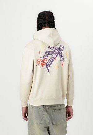 Cream-colored hoodie with a graphic design on the back, featuring bold text and shapes in purple, red, and yellow. Cotton blend material.