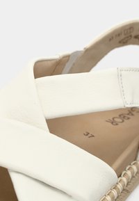 Λευκό δερμάτινο σανδάλι με υφαντή σόλα από τζούτ, σχεδιασμό με λουριά που διασταυρώνονται και λεία υφή. Διαθέτει μπεζ πάτο με ένδειξη μεγέθους.