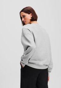 Grauer Sweatshirt mit lässiger Passform, gerippten Bündchen und Saum. Weicher Stoff, Rundhalsausschnitt und minimales Branding auf der Rückseite. Kombiniert mit schwarzen Hosen.