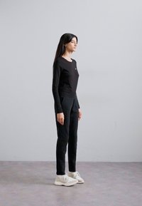 Haut noir à manches longues et pantalon noir, fabriqués dans un tissu lisse. Des baskets blanches avec des semelles texturées complètent la tenue.