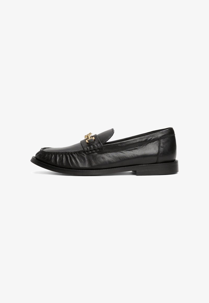 Mocassin en cuir noir à enfiler avec bout arrondi, détails cousus, semelle plate et petite boucle dorée en décoration sur le dessus.