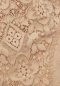 Beige kantstof met bloem- en geometrische patronen, kenmerkend door ingewikkelde details en een getextureerd oppervlak. De randen zijn afgewerkt met delicate stiksels.